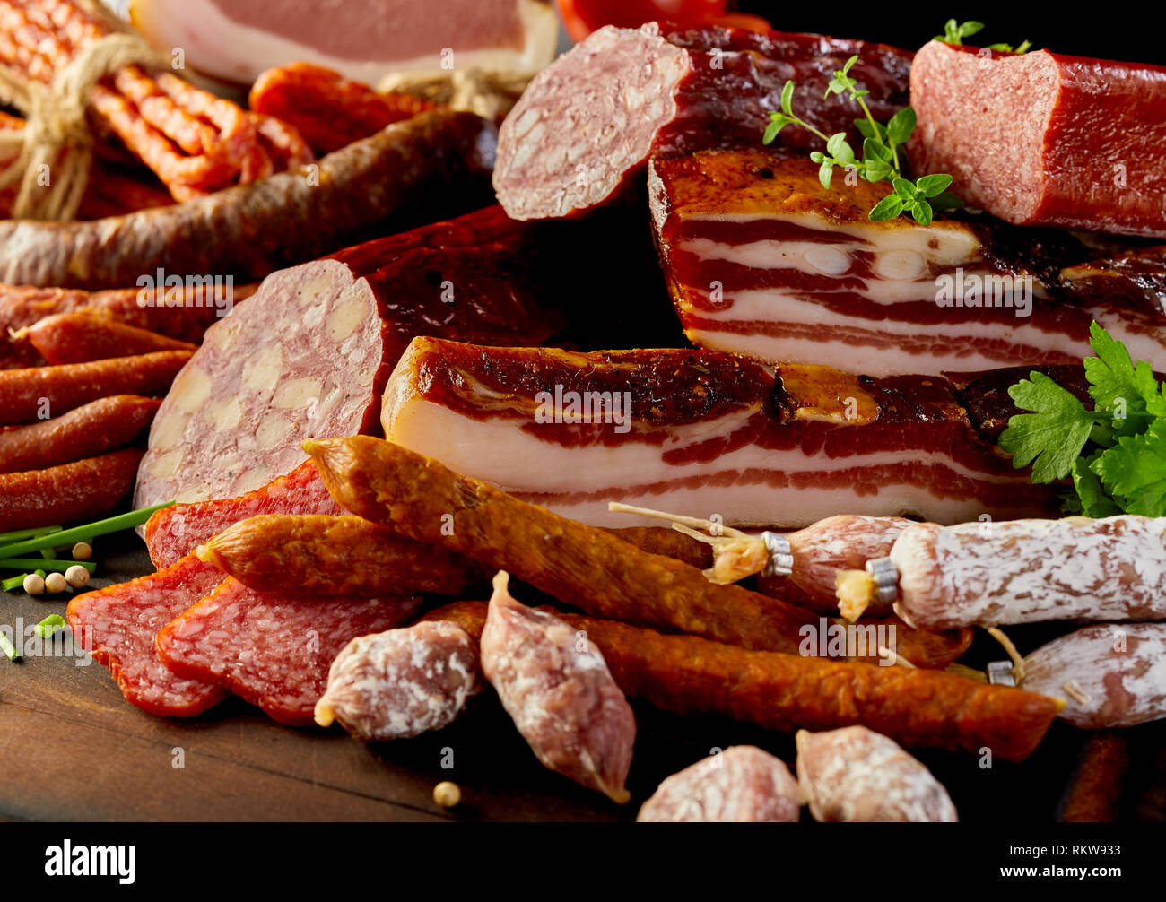 Selezione di specialità salsicce piccanti, salame affumicato e lardo visualizzata su un tavolo di legno con erbe fresche e grani di pepe in una vista ravvicinata Foto Stock