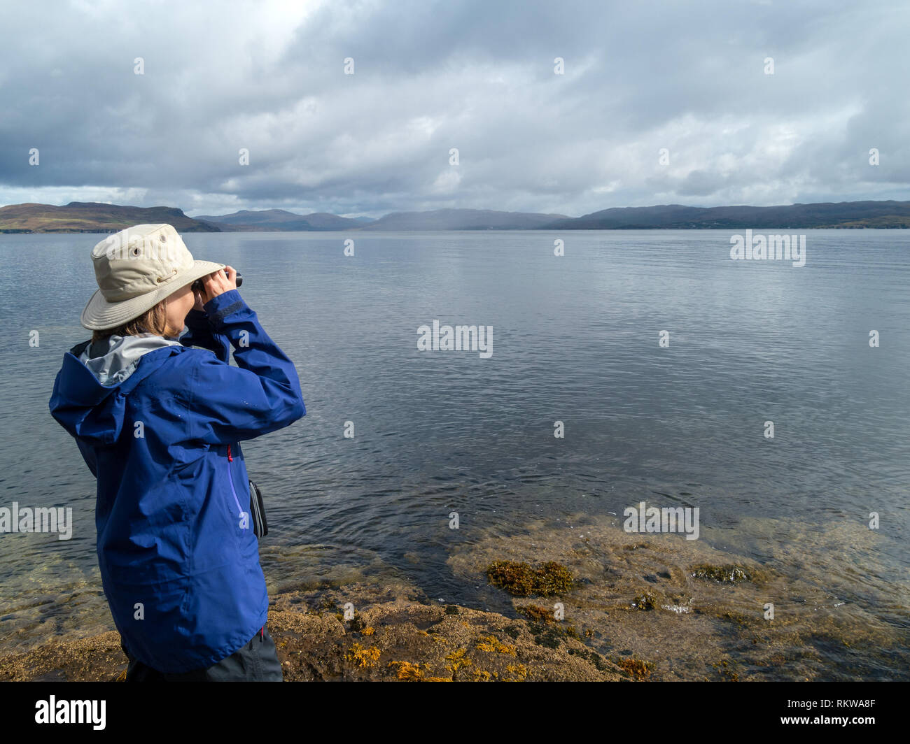 Donna che utilizza un binocolo per individuare gli animali marini in mare Loch Slapin, Isola di Skye in Scozia, Regno Unito Foto Stock