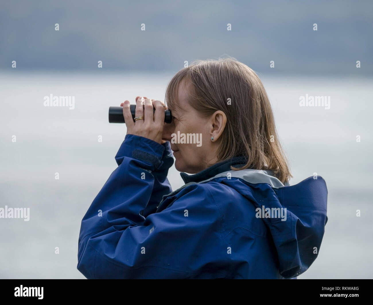 Donna che utilizza un binocolo per individuare gli animali marini in mare Loch Slapin, Isola di Skye, Scotland, Regno Unito Foto Stock