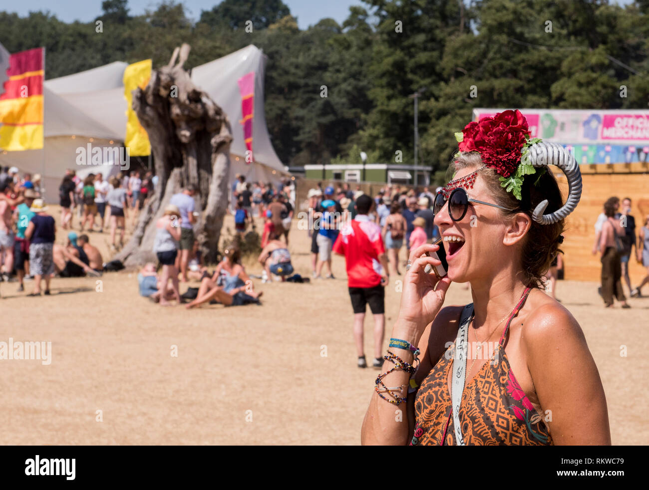 Un festival goer indossa uno strano cappello di un fiore e un corno di montone ride mentre parla con il suo telefono. Foto Stock