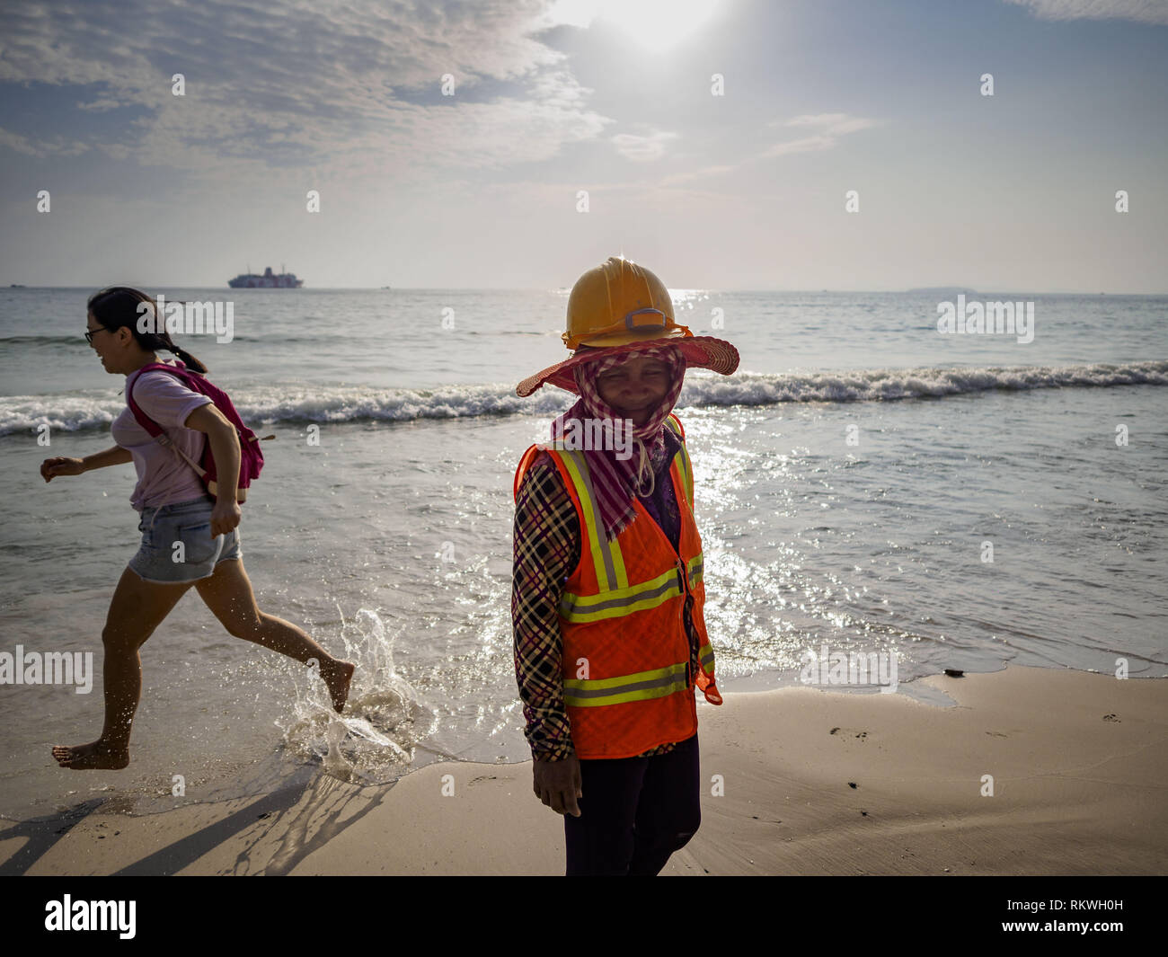 Sihanoukville, Preah Sihanouk, Cambogia. 12 Feb, 2019. Un cambogiano lavoratore edile passeggiate passato un turista cinese che corre lungo la spiaggia vicino il Blue Bay resort e lo sviluppo. Blue Bay cinese è un casino e resort essendo costruito in Sihanoukville. Ci sono circa 50 casinò cinese e resort hotel aperto o in costruzione in Sihanoukville. I CASINÒ sono cambiando la città, una volta che una sonnolenta porta sul sudest asiatico del ''backpacker trail'' in una fiorente città. Il cambiamento è in arrivo con un costo però. Molti residenti cambogiano di Sihanoukville hanno perso le loro case per far posto alla Foto Stock