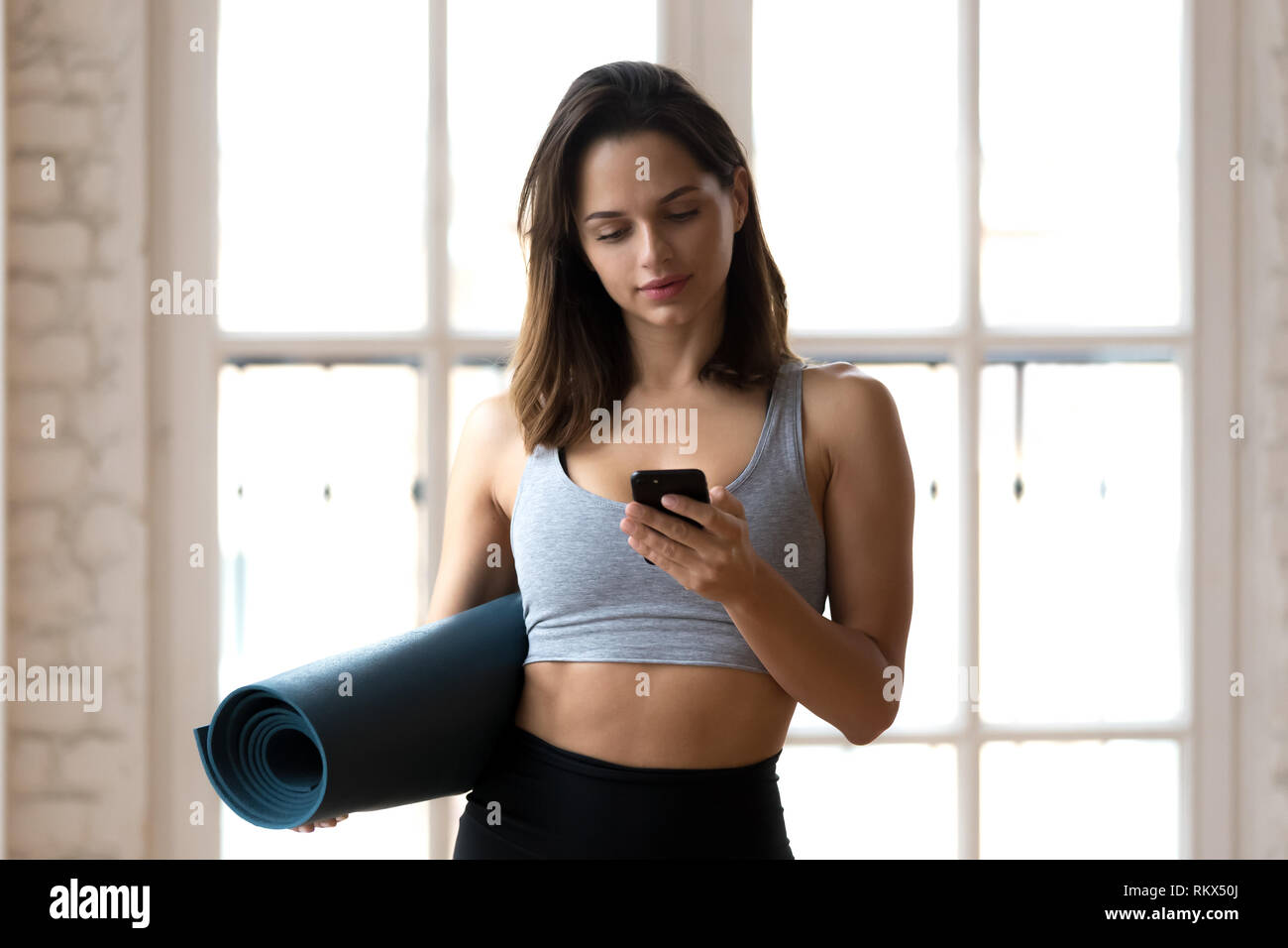 Montare atleta femminile utilizza lo smartphone in attesa per la formazione Foto Stock