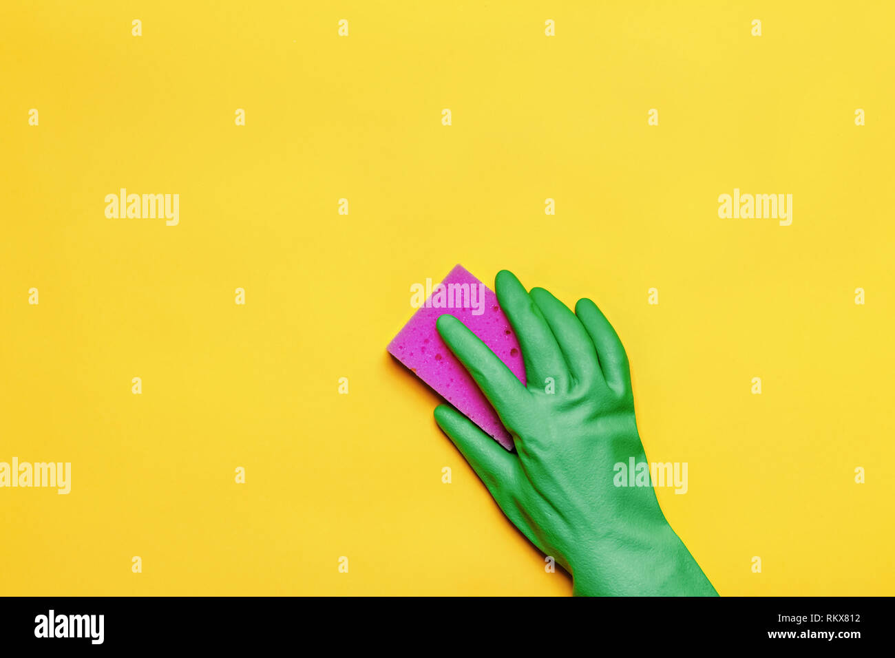 Una mano in una gomma di guanto protettivo con una spugna rosa su sfondo giallo. Il concetto di pulizia. Foto Stock