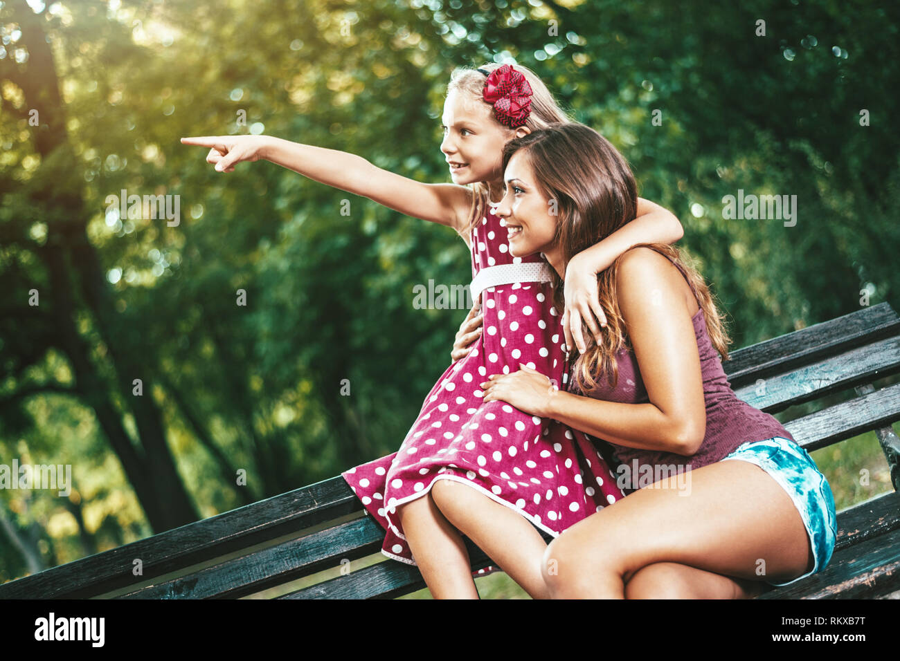 Felice carino bambina sta giocando nel parco con sua madre qualcosa di puntamento. Essi sono abbraccia ogni altra e sorridente. Foto Stock