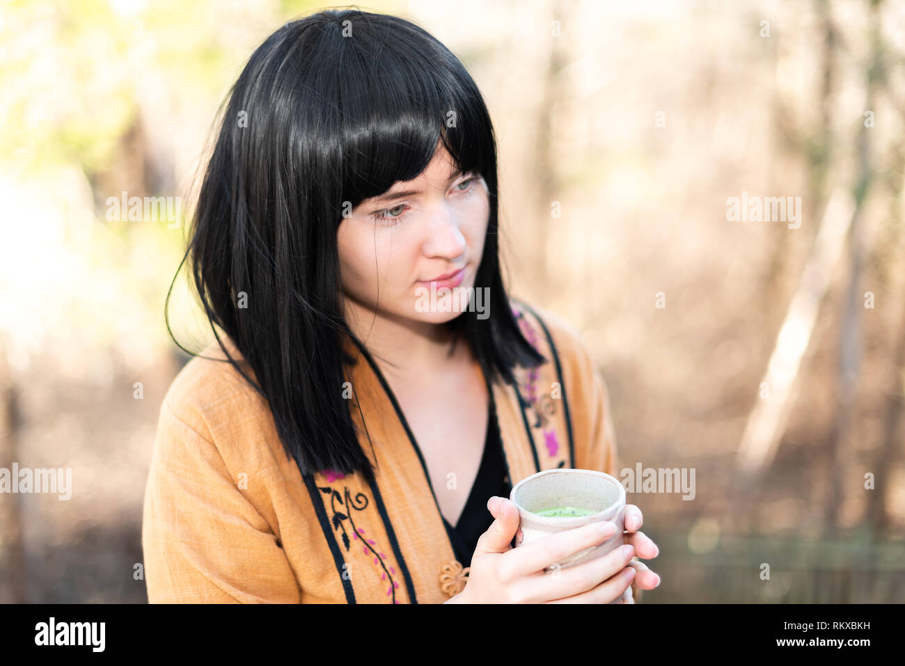 Donna che mantiene tè verde Matcha cup in fuori in giardino nel cortile con il giovane ragazza capelli neri e asiatici alla ricerca di vestiti Foto Stock