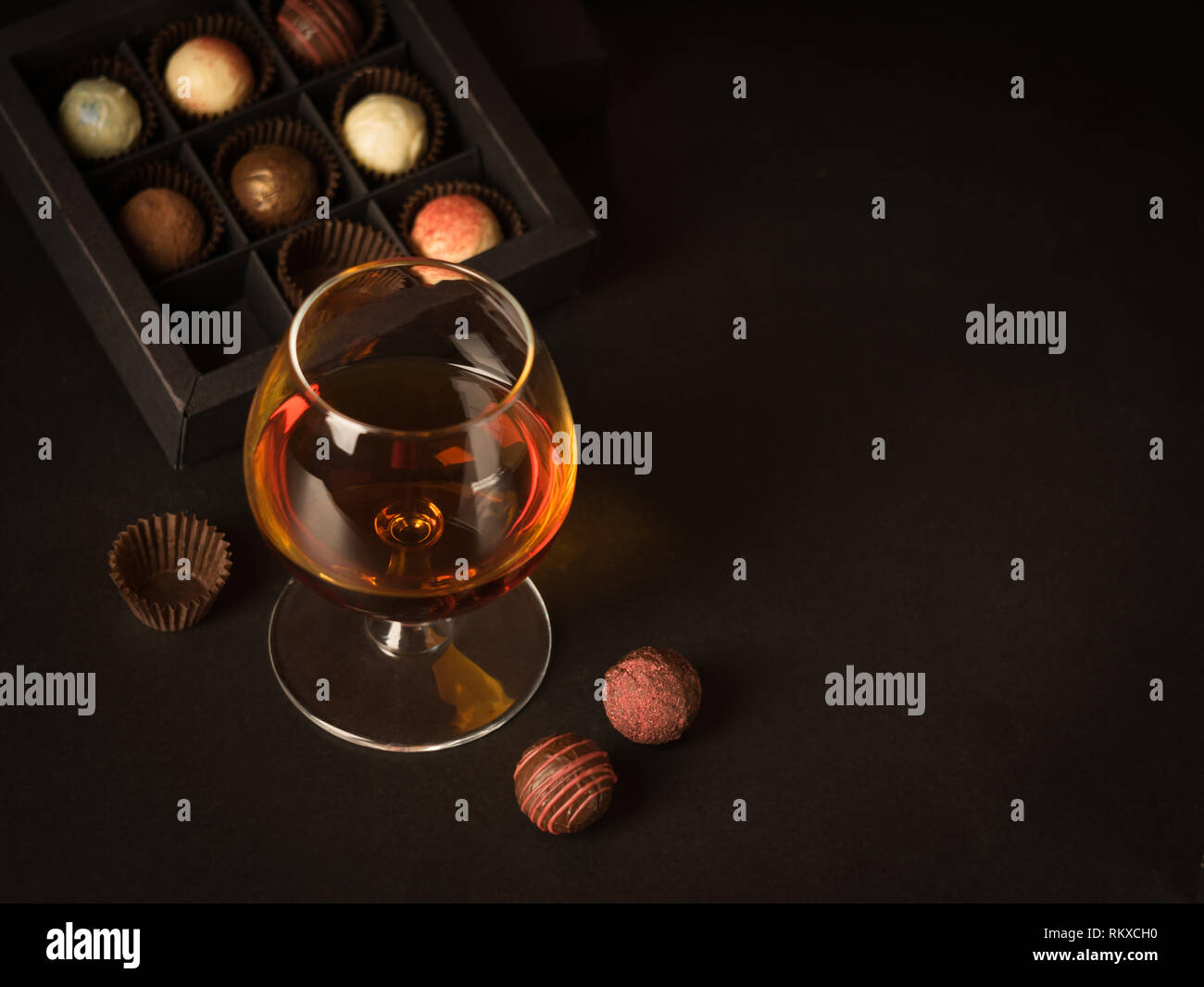 Un bicchiere di brandy cioccolato e caramelle su uno sfondo scuro. La bevanda alcolica e cioccolato elite concetto alimentare. Foto Stock