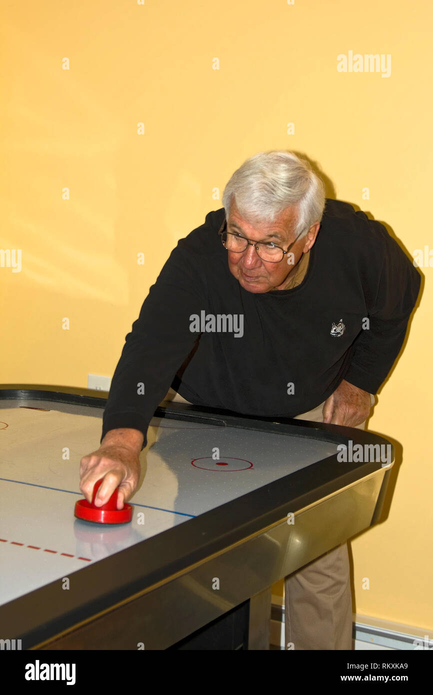 Senior uomo giocando air hockey; Gioco; concorrenza; home ricreazione; occhiali; i capelli grigi, concentrandosi espressione seria, verticale; signor Foto Stock