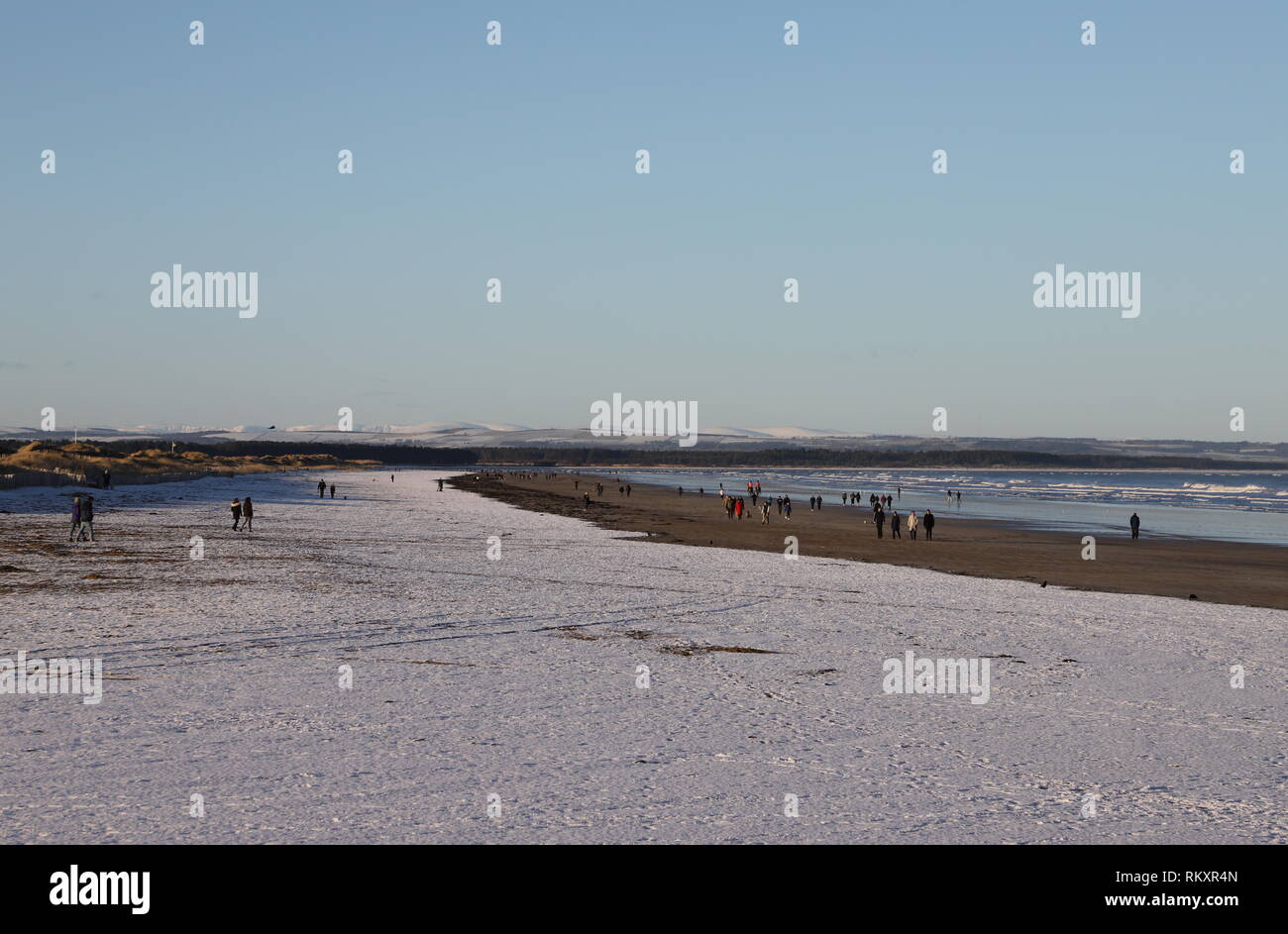 La gente che camminava sul West Sands Beach St Andrews con lontane cime coperte di neve in Angus Glens St Andrews Fife Scozia Febbraio 2019 Foto Stock