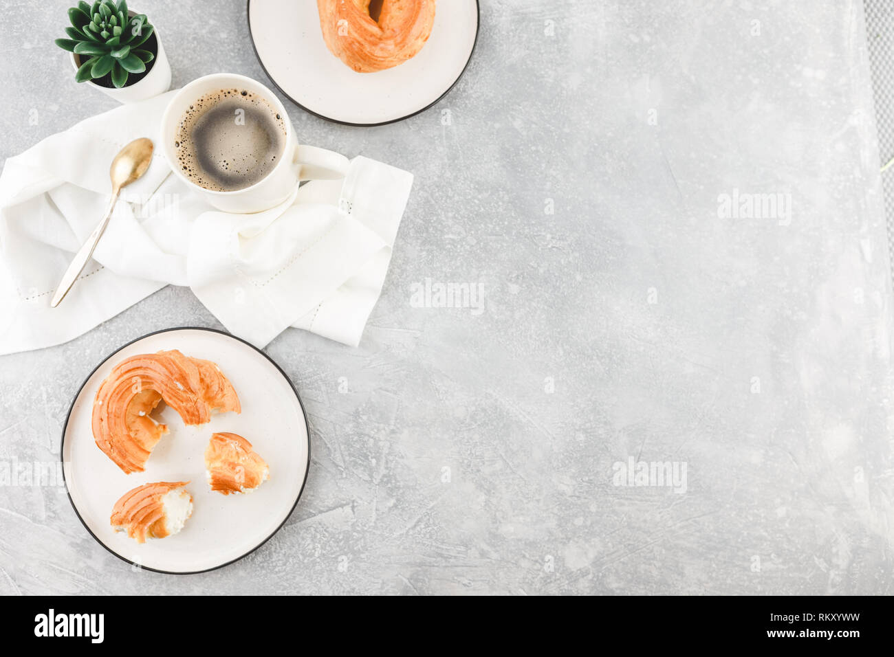 La prima colazione con soffio di crema anelli - bignè e tazza di caffè nero su uno sfondo luminoso Foto Stock