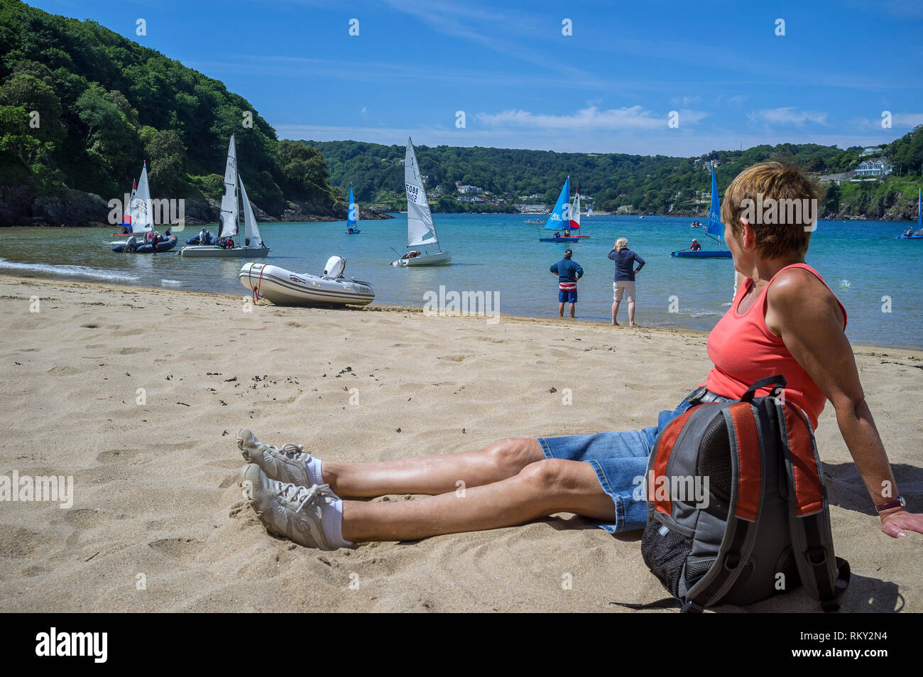 Una donna che guarda le attività di vela nell'estuario di Salcombe al largo di Mill Bay, una spiaggia riparata e sabbiosa popolare tra turisti e locali. Devon, Regno Unito Foto Stock