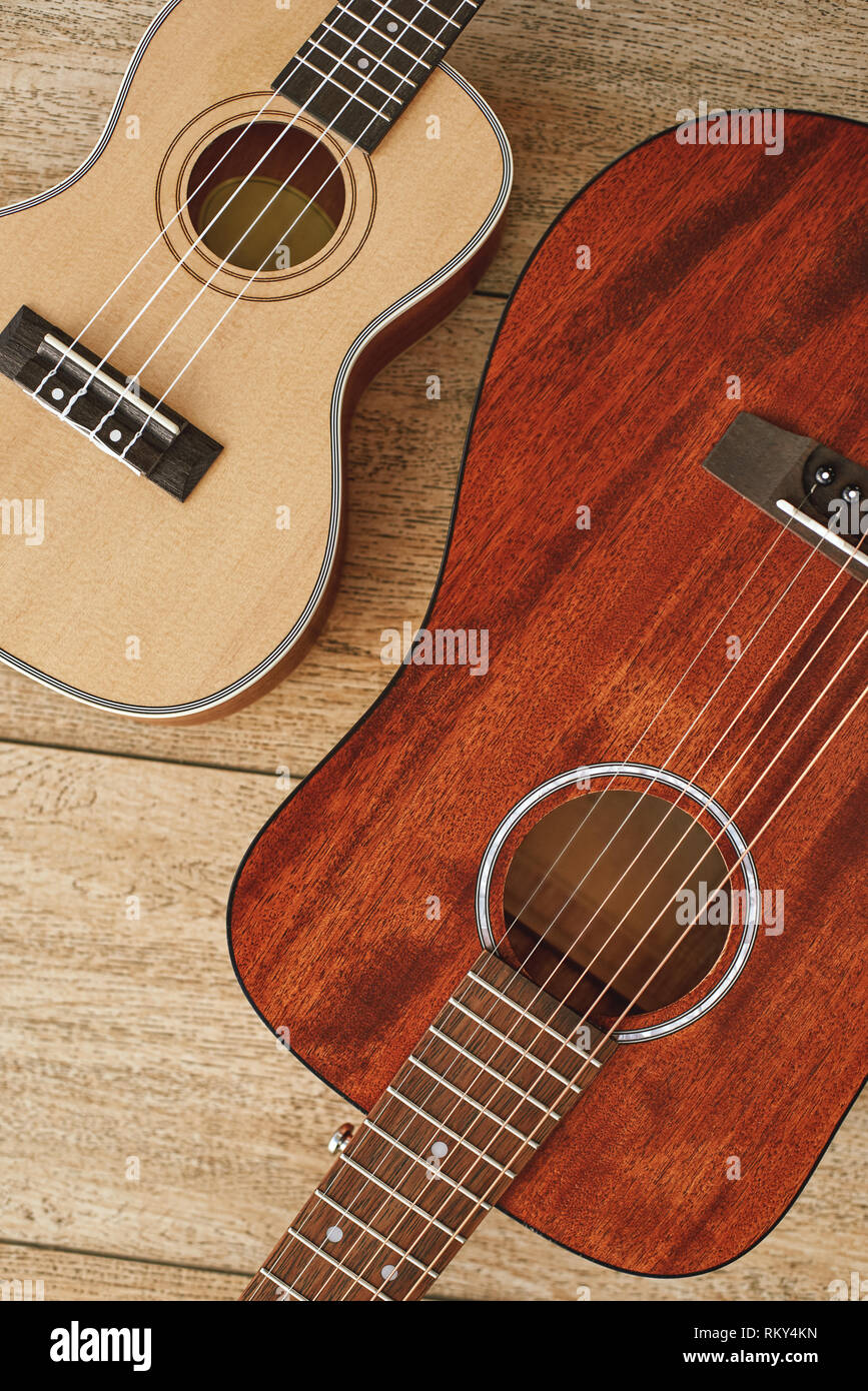 Musica dal cuore. Verticale in alto vista di acustica e ukulele chitarre che giace vicino a ogni altro su pavimento di legno. Il concetto di musica. Strumenti musicali Foto Stock