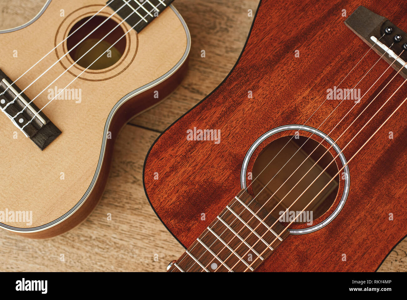 Ideale coppia musicale. Vista superiore dell'acustica e ukulele chitarre che giace vicino a ogni altro su pavimento di legno. Strumenti musicali. Attrezzature musicali. Negozio di musica Foto Stock
