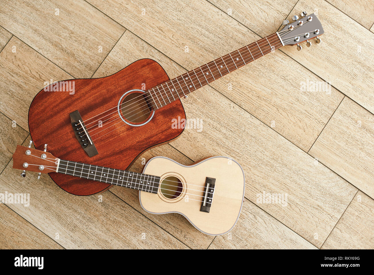 Strumenti musicali di sottofondo. Vista superiore dell'acustica e ukulele chitarre che giace vicino a ogni altra contro il pavimento in legno. Attrezzature musicali. Negozio di musica Foto Stock