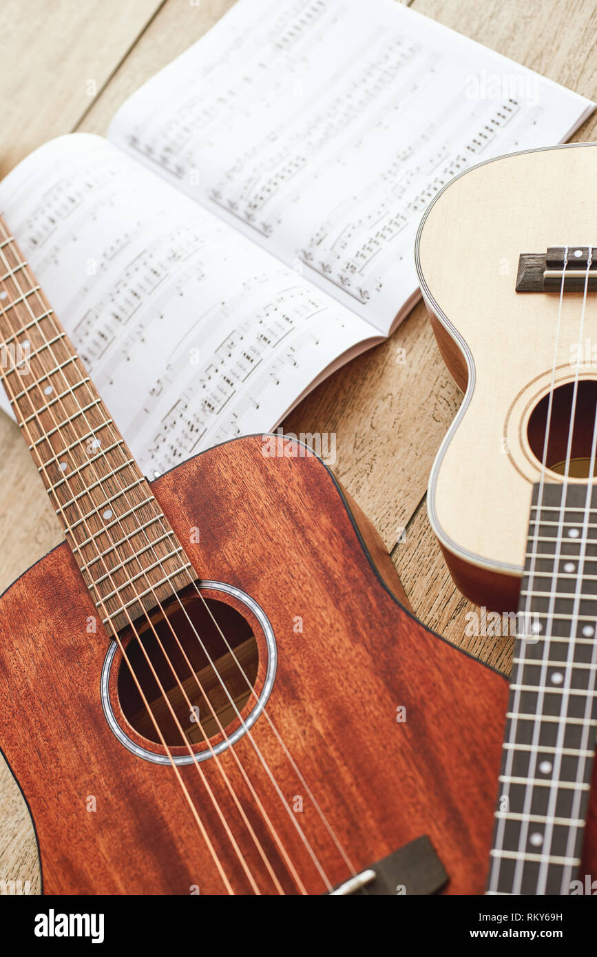 Imparare a suonare la chitarra. Chiudere verticale fino foto di acustica e ukulele chitarre sdraiato sul pavimento in legno con note musicali. Vista dall'alto. Attrezzature musicali. Negozio di musica. Strumenti musicali Foto Stock