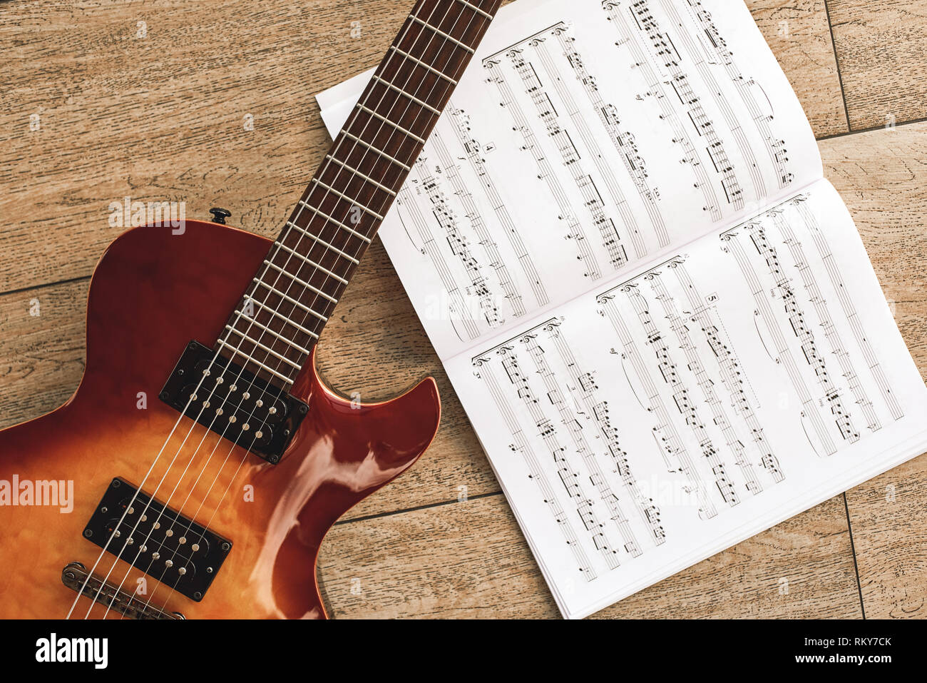 Il suono della musica rock. Vista superiore della bella chitarra elettrica con note musicali contro di sfondo di legno. Strumenti musicali. Educazione musicale. Foto Stock