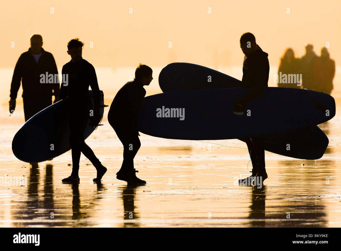 Surfers che trasportano le tavole da surf stagliano nel tardo pomeriggio la luce del sole. Foto Stock