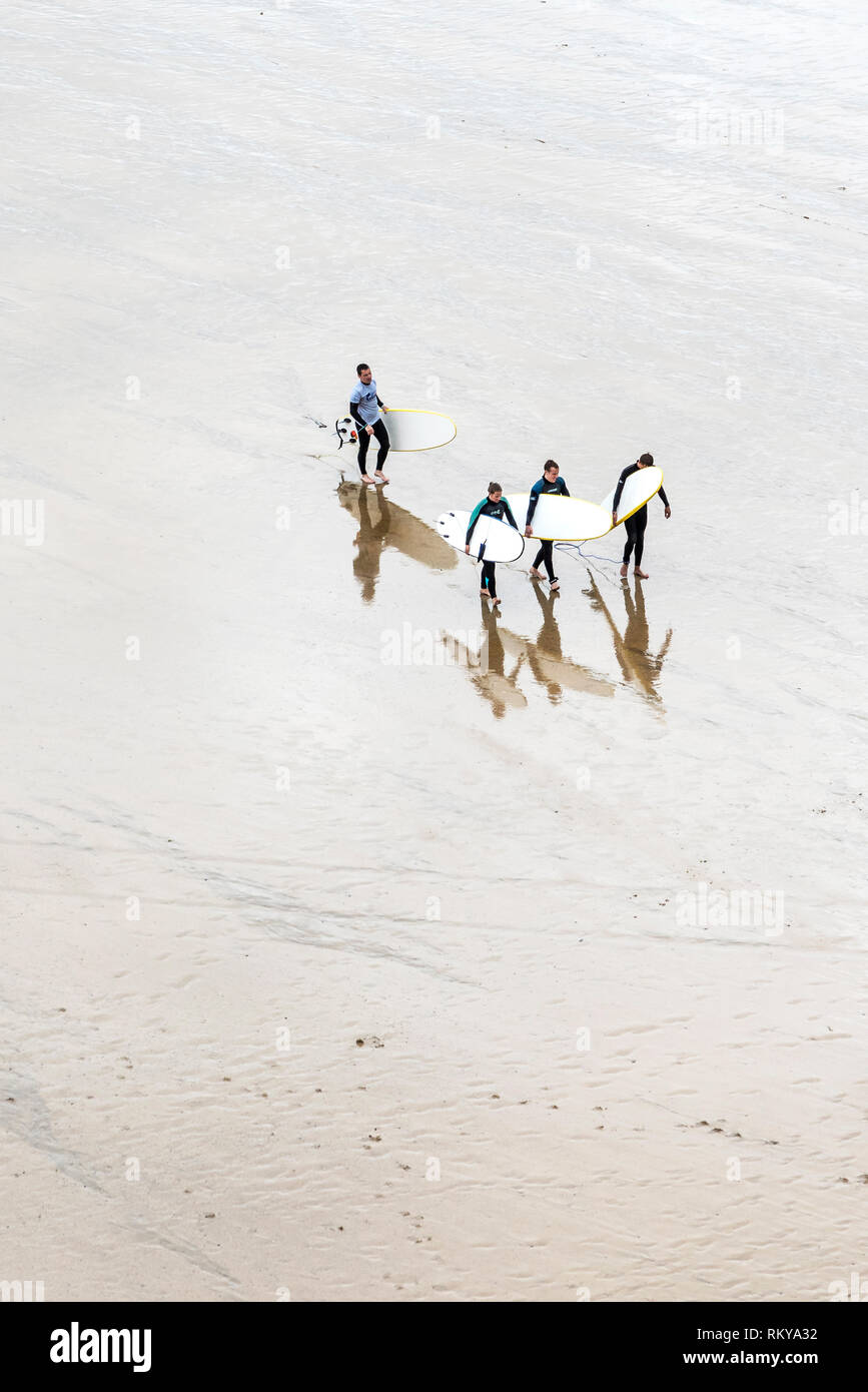 Una vista aerea di surfers e loro surf istruttore portando le loro tavole da surf dopo una lezione di surf a Newquay in Cornovaglia. Foto Stock