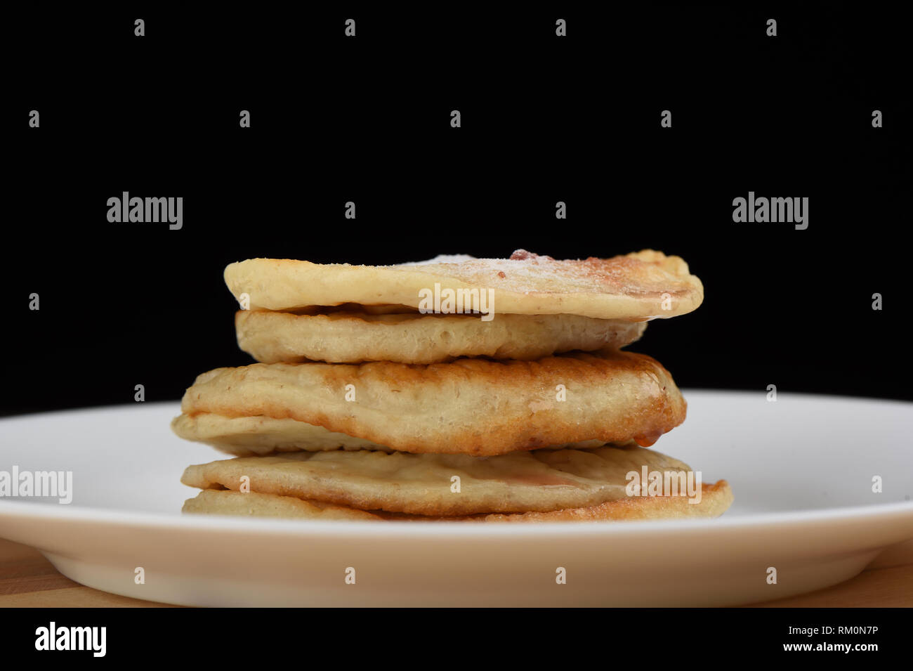 Una pila di pancake di avena in una piastra bianca su uno sfondo di legno, di fronte a uno sfondo nero Foto Stock