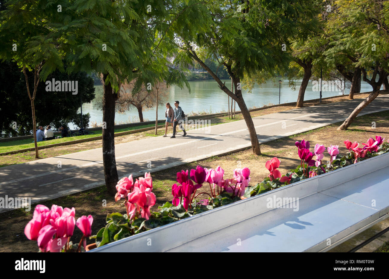 Una giovane coppia camminando accanto al fiume Guadalquivir in un caldo giorno di febbraio a Siviglia, Spagna Foto Stock