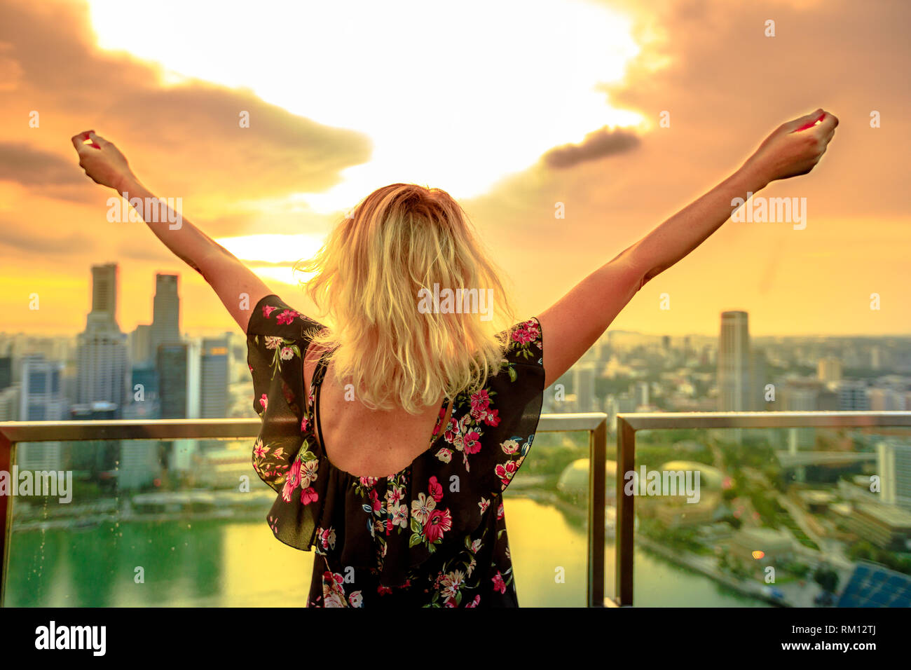 Carefree donna bionda guardando il panorama dalla terrazza sul tetto in Marina Sud, Singapore. Vista aerea del paesaggio urbano skyline al tramonto. Stile di vita turistico a Foto Stock
