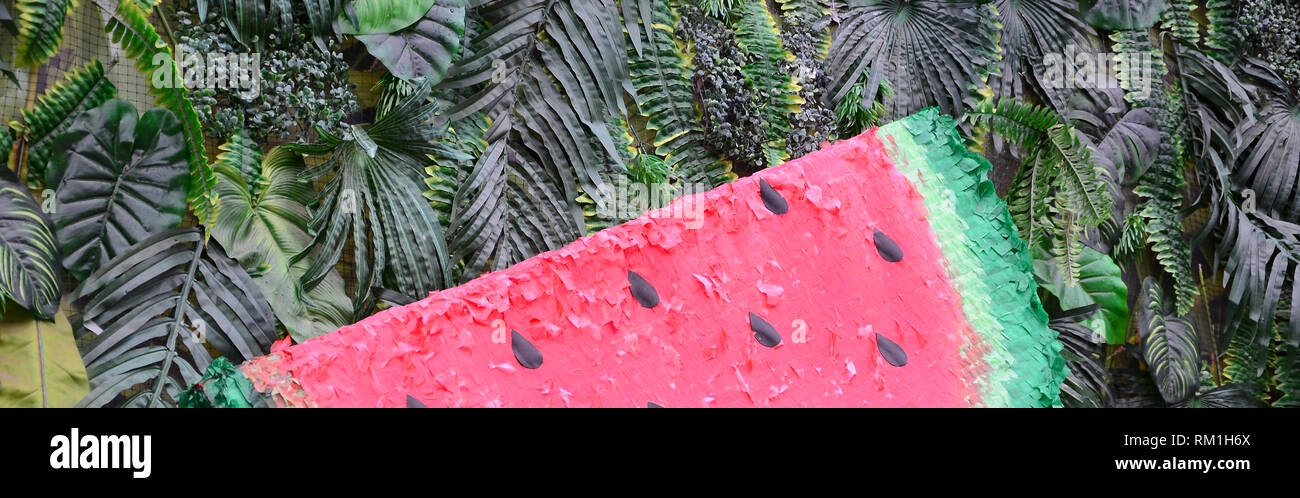 Modello di tropicale con la giungla di foglie e frutti di anguria sfondo floreale. Anguria in plastica con strato di foglie di palma Foto Stock