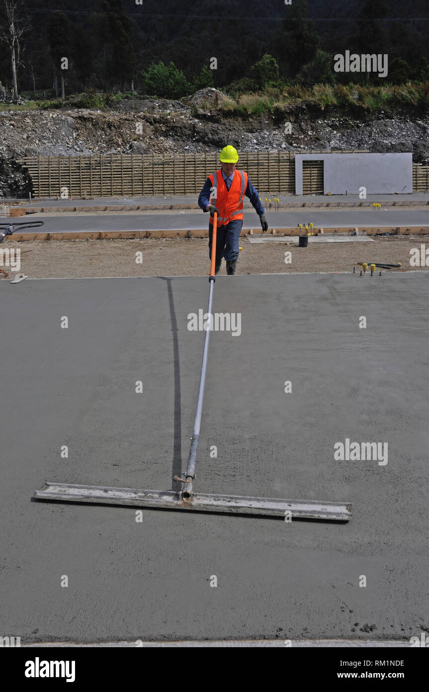 Un builder utilizza una lunga gestite cazzuola a galleggiare fuori un umido lastra di calcestruzzo per un edificio di grandi dimensioni Foto Stock