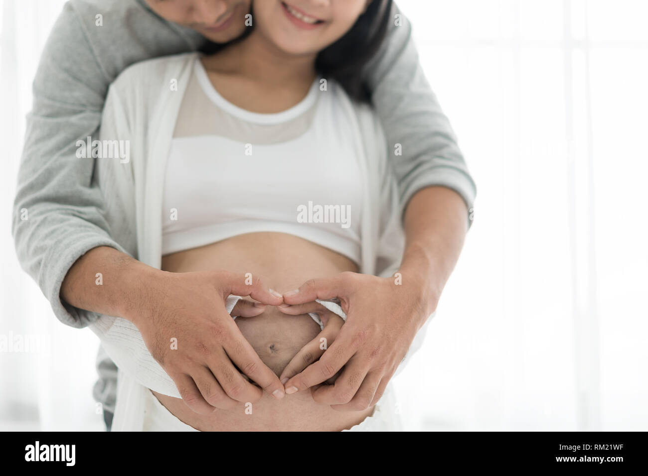 Asian bella donna incinta e il suo bel marito abbracciando la pancia. Amore giovane mani fare un cuore sulla pancia in gravidanza. Foto Stock