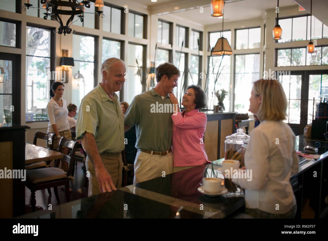 Senior essendo donna affettuosa verso il suo nipote adolescente come suo marito gli ordini un caffè in un bar. Foto Stock