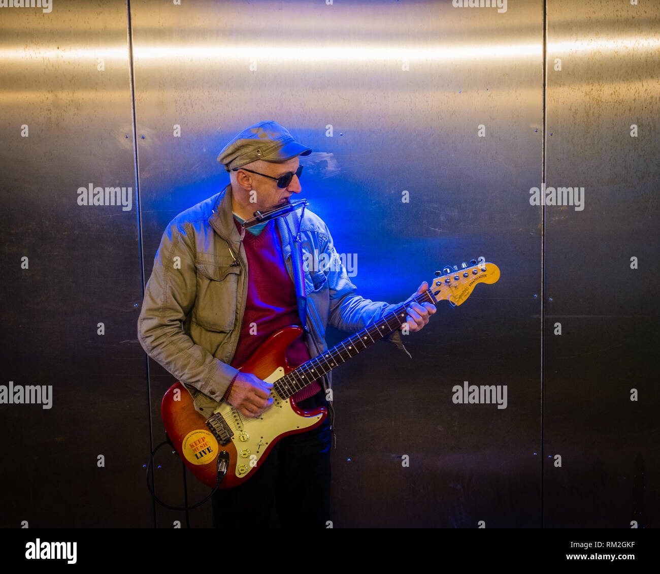 Suonatore ambulante maschio a suonare la chitarra in neon blu accesa sottopassaggio Fort William highlands scozzesi Scozia Scotland Foto Stock