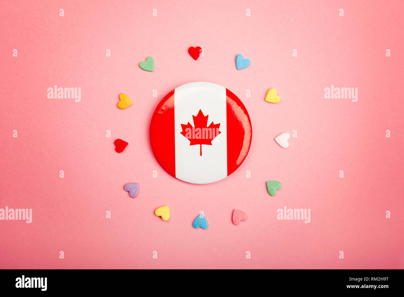 Felice giorno Canada biglietto di auguri con la bandiera canadese nel centro medio e molte caramelle colorate cuori attorno ad esso su coralli viventi sfondo rosa. Multicu Foto Stock