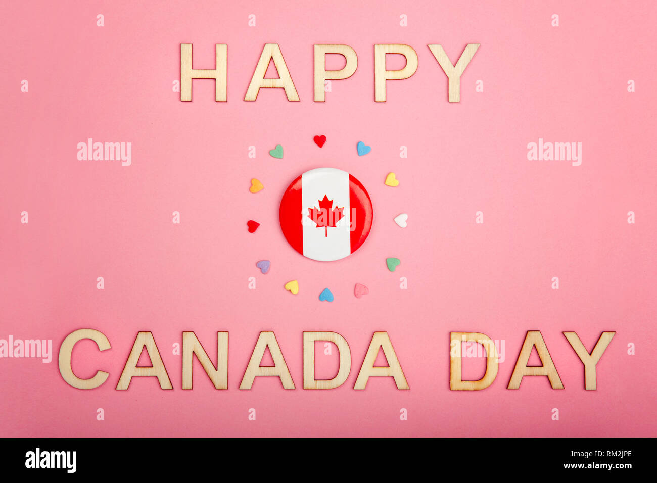 Happy Canada Day greeting card con lettere in legno. Parole e bandiera canadese con molte caramelle cuori attorno ad esso su coralli viventi sfondo rosa. Multic Foto Stock
