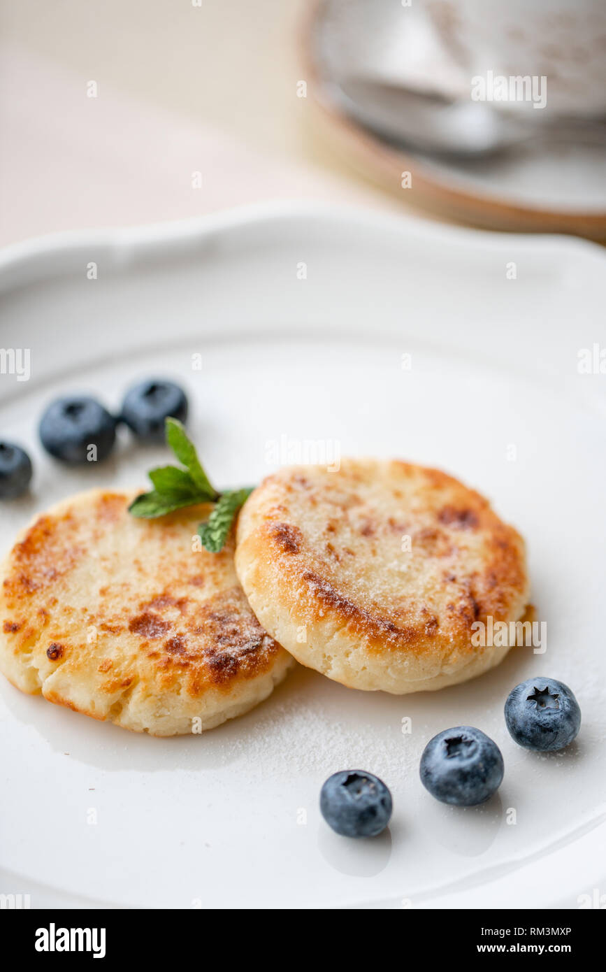 Cheesecake, ai mirtilli freschi e cappuccino. Cottage cheese pancakes o frittelle di cagliata sulla piastra bianca. Sana dieta e colazione all'alba Foto Stock