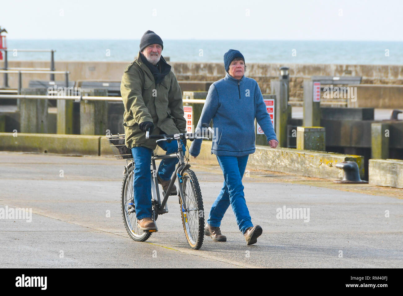 West Bay, Dorset, Regno Unito. Il 13 febbraio 2019. Regno Unito Meteo. Fumoso sole riscalda un ciclista e walker a West Bay nel Dorset che sono avvolti ben dopo una fredda per iniziare la giornata. Le temperature sono impostate a salire come venti da sud dai tropici sono impostati a soffiare di tutta la contea nel giro di un paio di giorni portando temperature sopra la media. Credito Foto: Graham Hunt/Alamy Live News Foto Stock