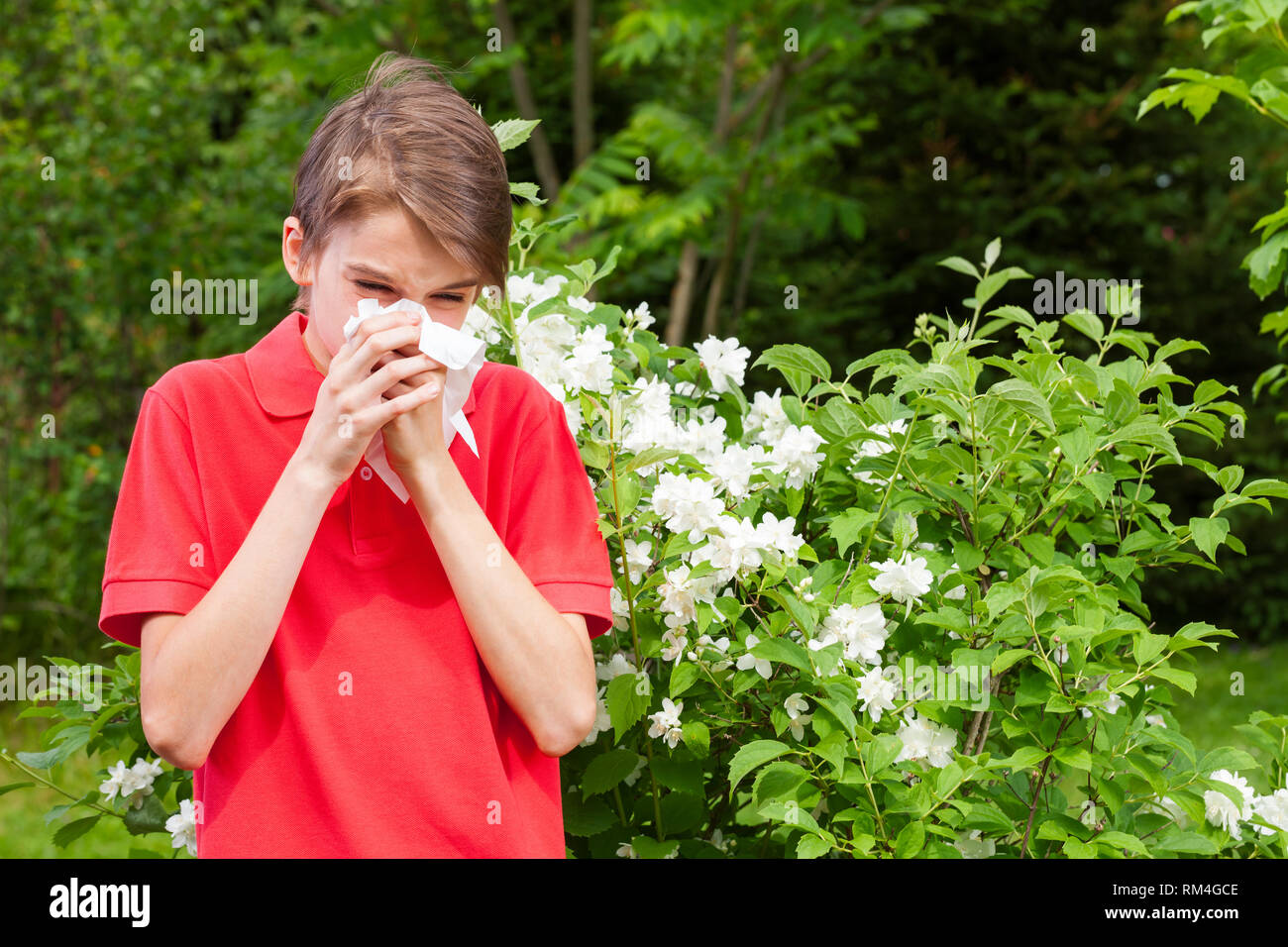 Ragazzo adolescente con influenza stagionale soffia il naso su un tessuto in un giardino di Primavera - stagione concetto di infezione Foto Stock