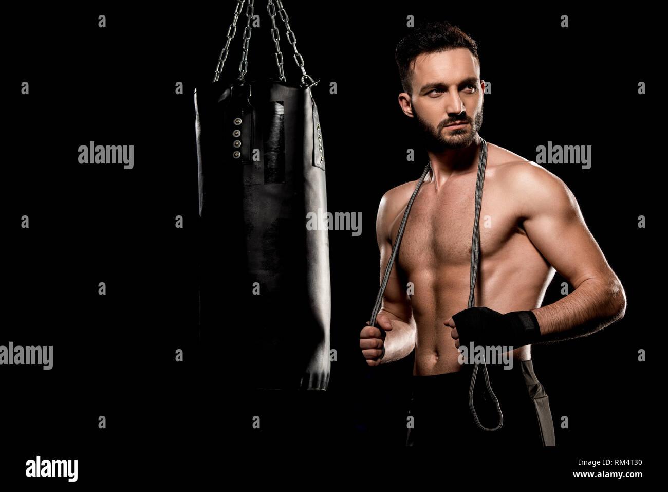 Bello il boxer in piedi con salto con la corda nei pressi di sacco da boxe isolato su nero Foto Stock