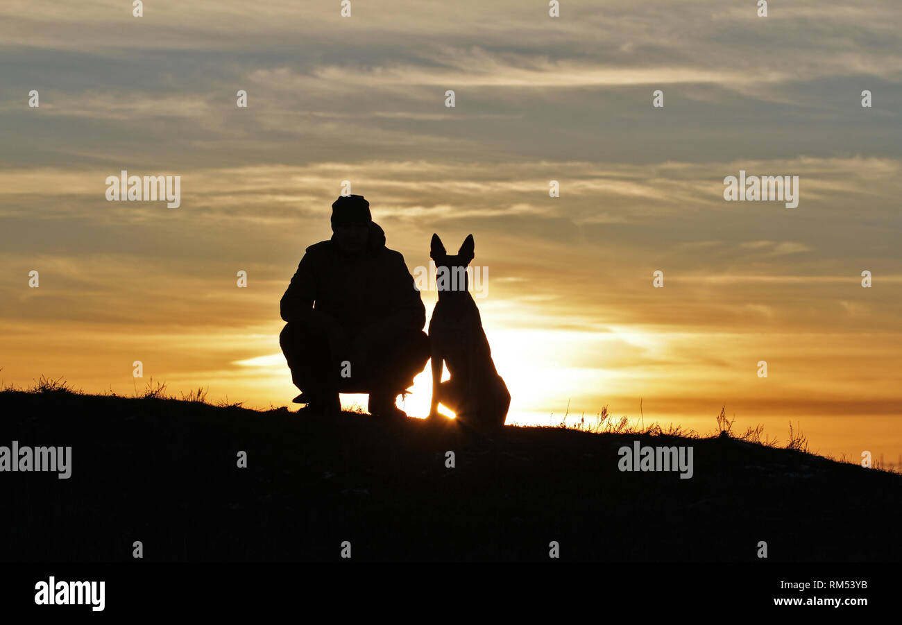 Uomo e cane contro lo sfondo di un incredibile tramonto Foto Stock