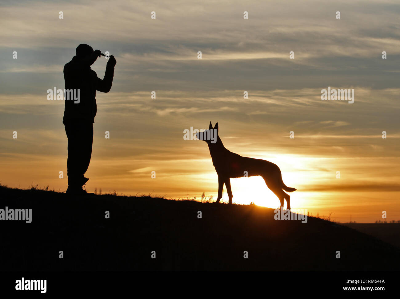 Uomo e cane contro lo sfondo di un incredibile tramonto Foto Stock