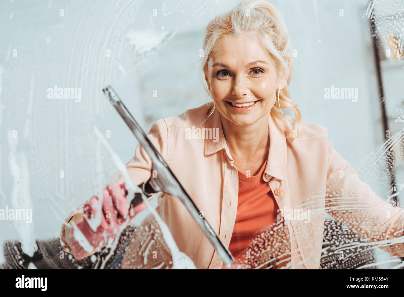 Meravigliosa donna senior con tergicristallo vetro mentre la finestra di pulizia Foto Stock