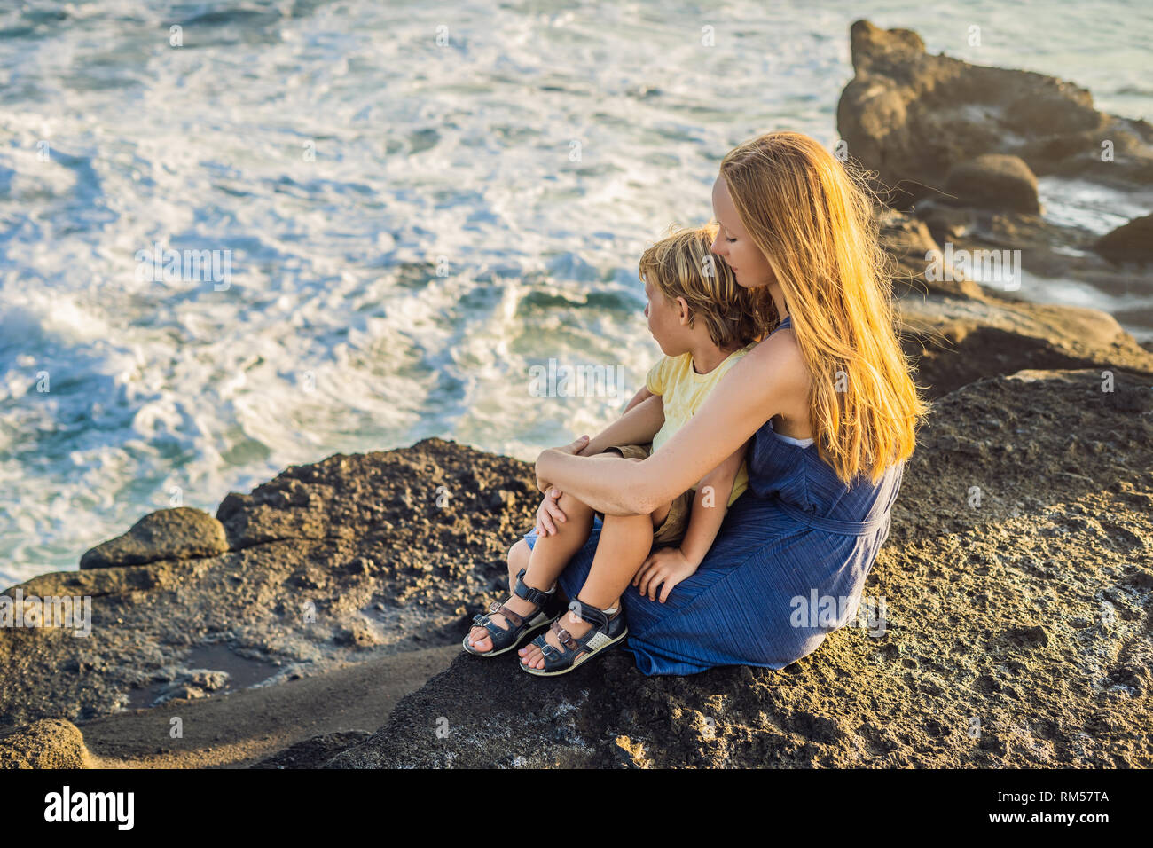 Madre e figlio sono seduti su una roccia e guardando il mare. Ritratto di turisti viaggio - MOM con i bambini. Positive le emozioni umane, uno stile di vita attivo. Felice Foto Stock