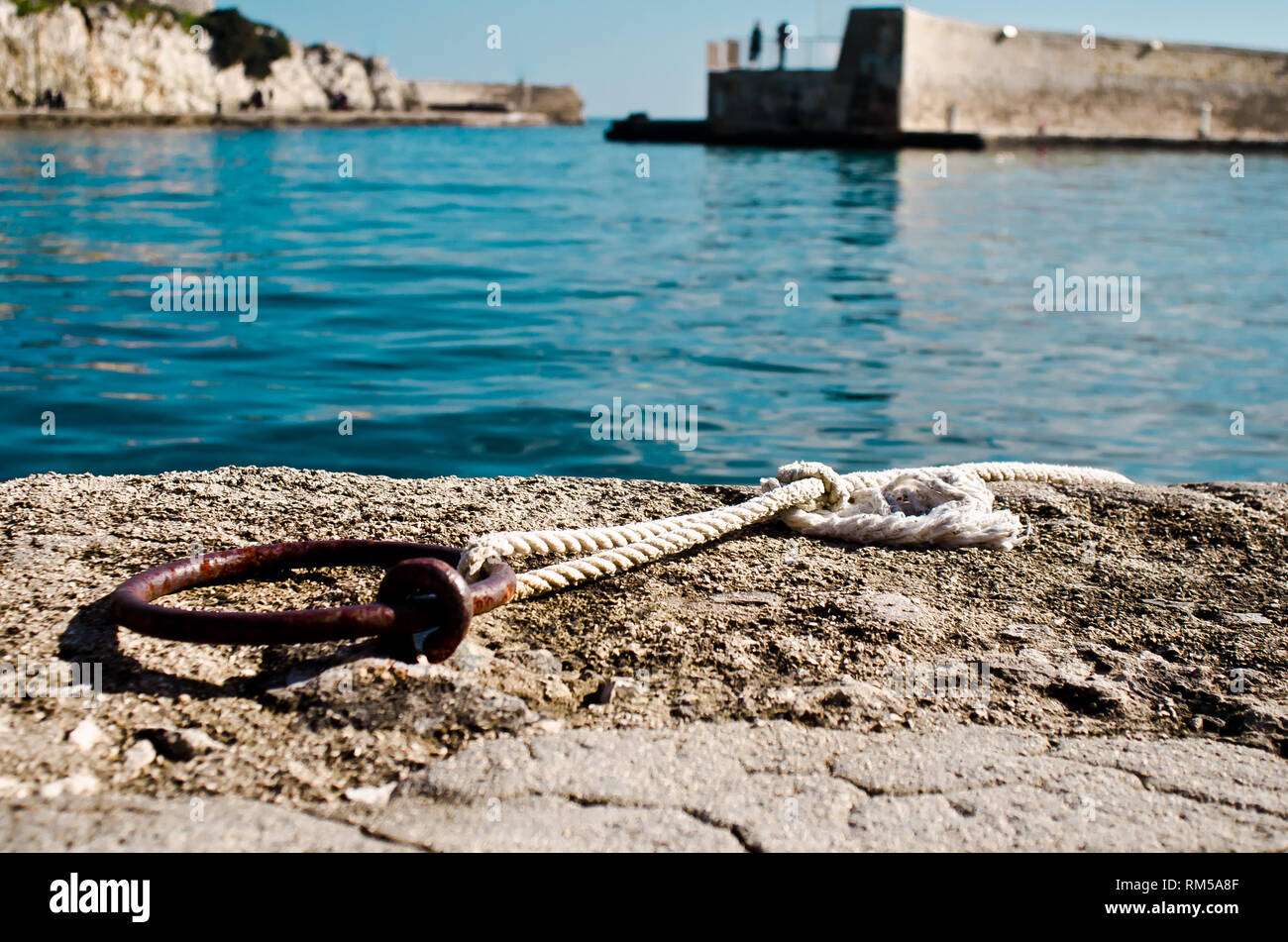 Anello arrugginito con corda bianca in un dock lungo il mare Mediterraneo Foto Stock