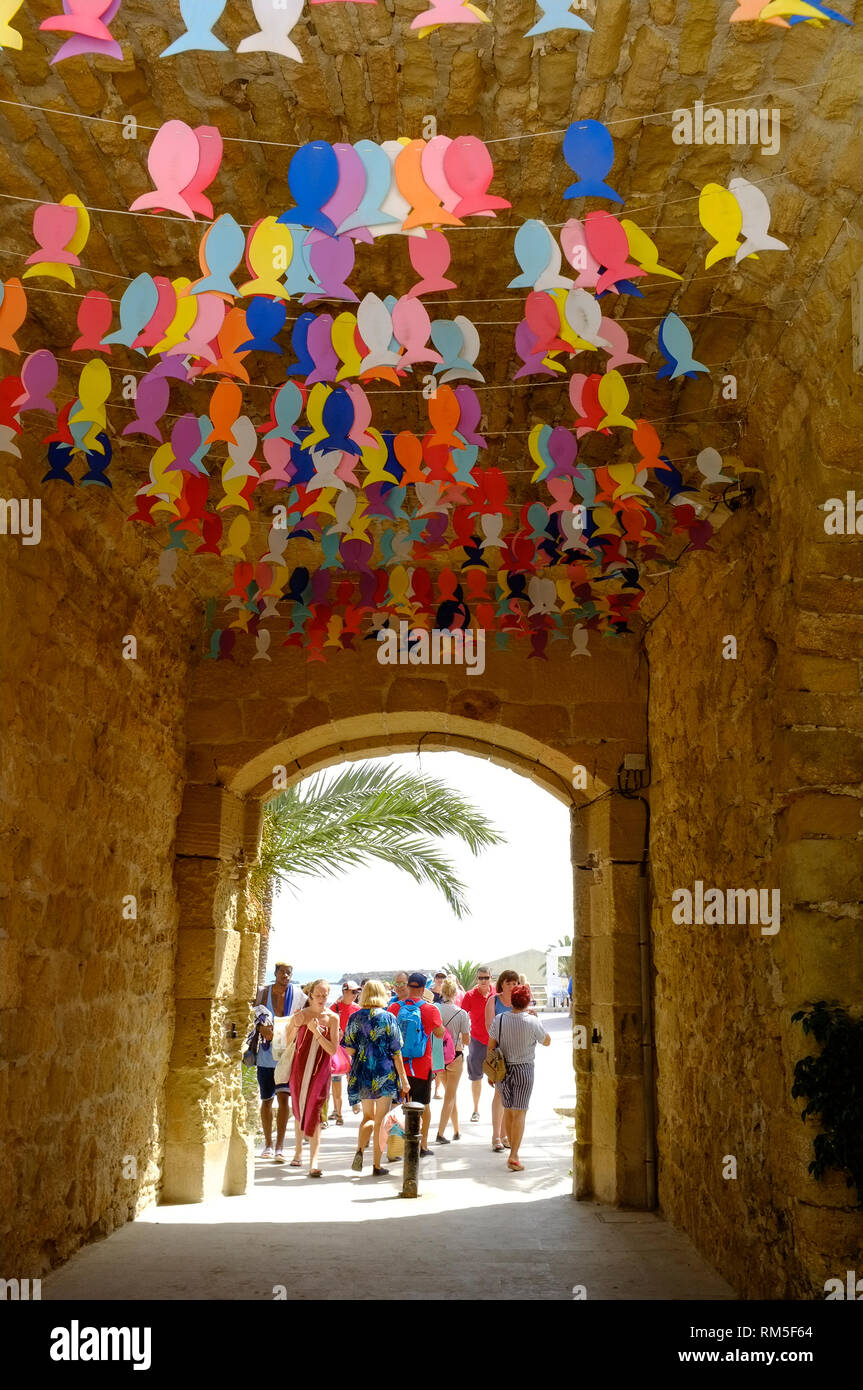 Trippers giorno e turisti a piedi attraverso la addobba portone che conduce nella strada principale su isola di Tabarca, Alicante, Spagna Foto Stock