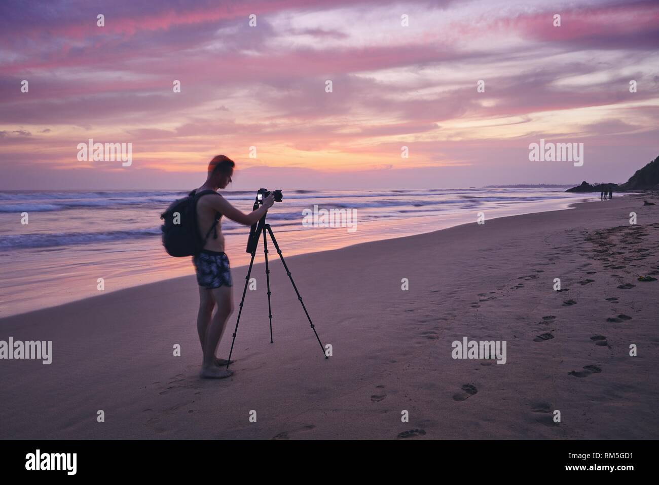 Giovane uomo fotografare con il cavalletto in spiaggia dopo il tramonto. Fotografo in movimento sfocata. Foto Stock