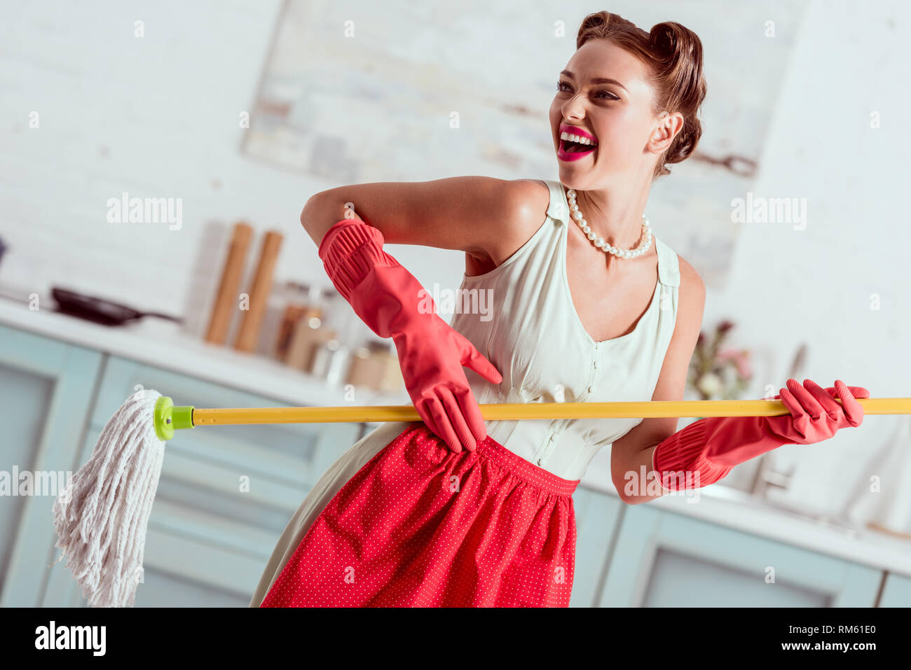 Allegro pin up girl in red grembiuli e guanti di gomma ballando con mop giallo Foto Stock