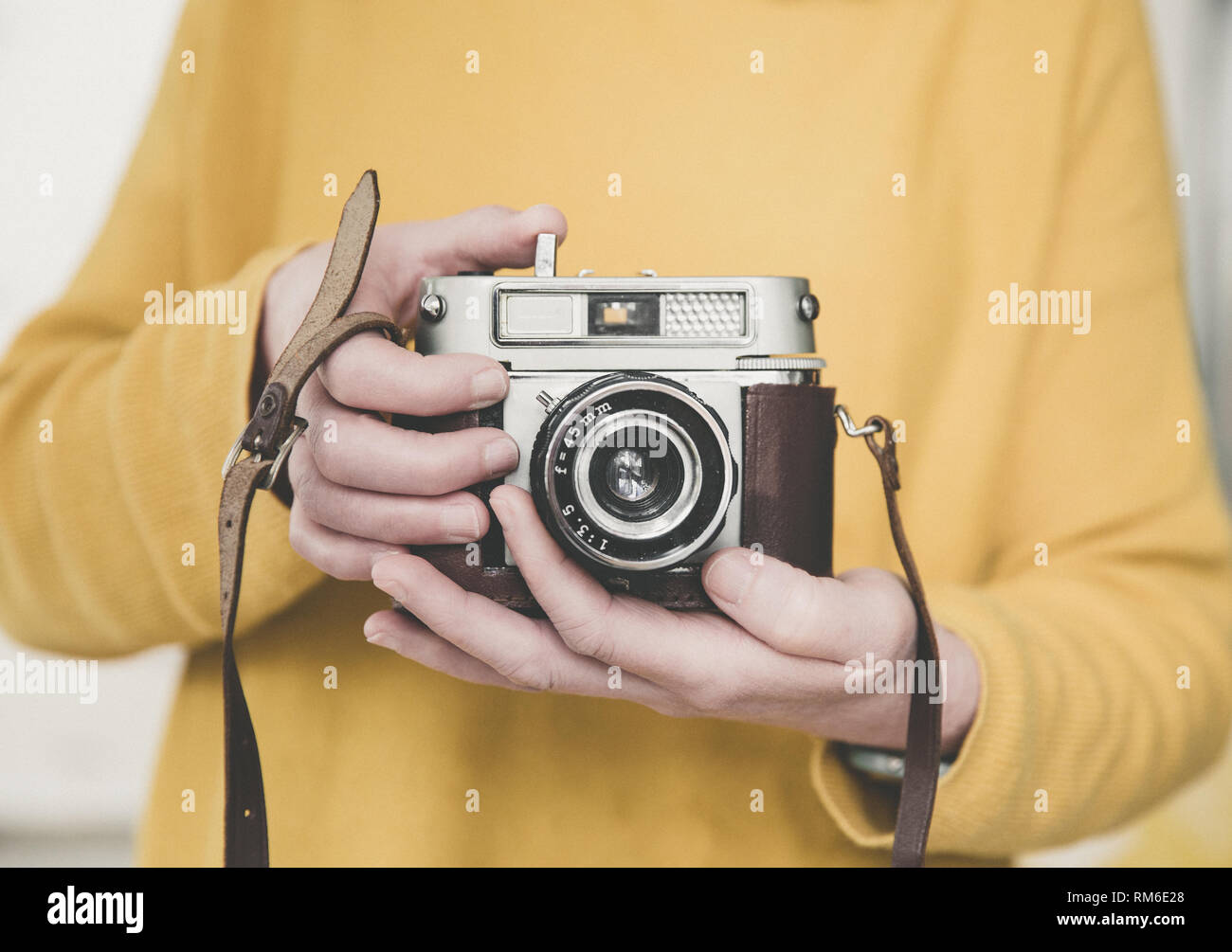 Una sezione mediana di un fotografo femmina giallo che indossa mentre tiene un vintage, 35mm Fotocamera con spazio di copia Foto Stock