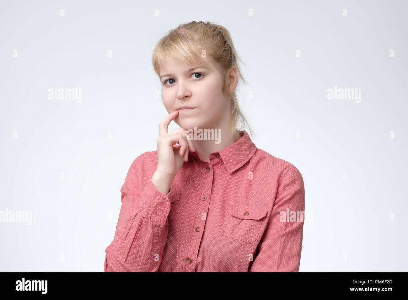 Pensando donna bionda in maglia rosa interrogandosi su qualcosa Foto Stock