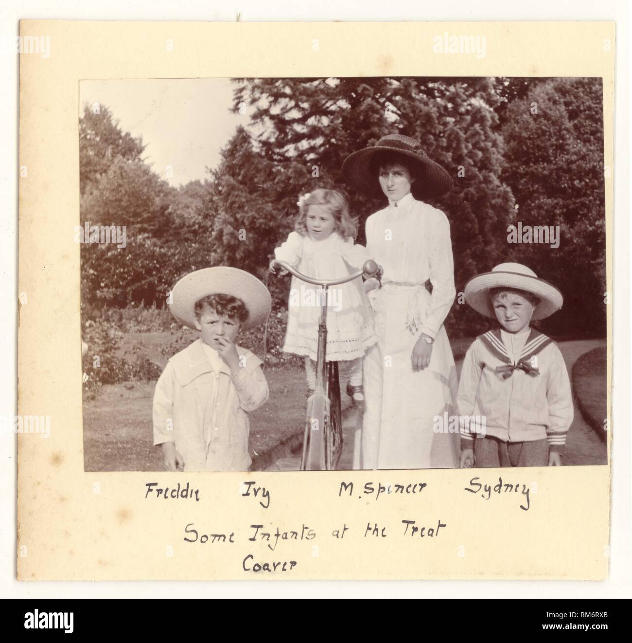 Edwardian fotografia di un attraente madre in un bianco estate camicetta e gonna a piedi con lei i bambini nel parco o giardino. Il bambino più in giovane età è bilanciato su madre della bicicletta,i ragazzi di usura marinaio di moda abiti e cappelli di paglia, circa 1910, U.K. Foto Stock