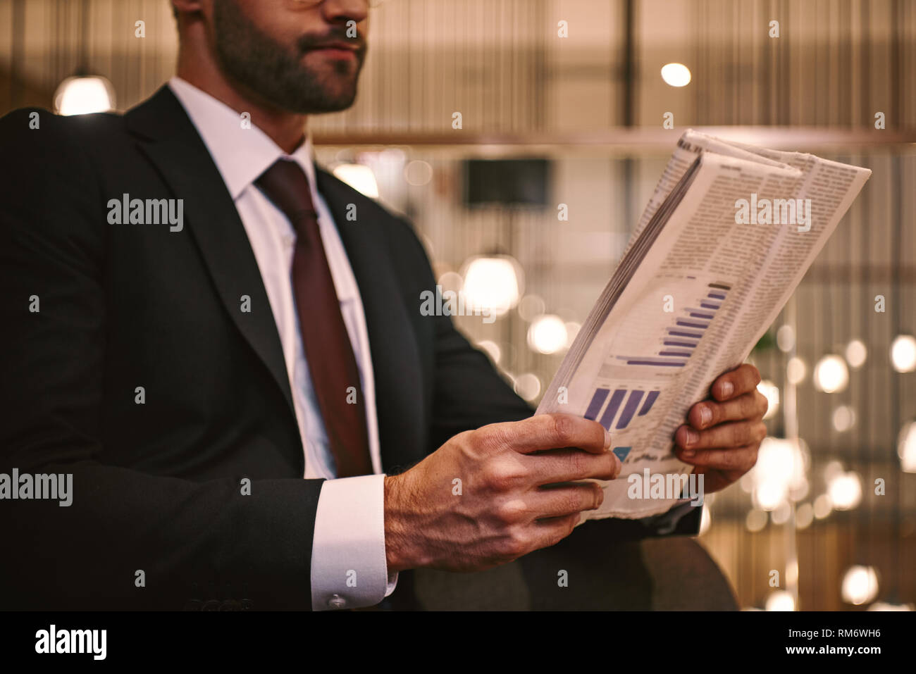 In attesa di partner aziendale. Close-up del giovane uomo che legge il giornale mentre seduti al ristorante dell'hotel vicino a valigia. Lusso a interiour backbround Foto Stock
