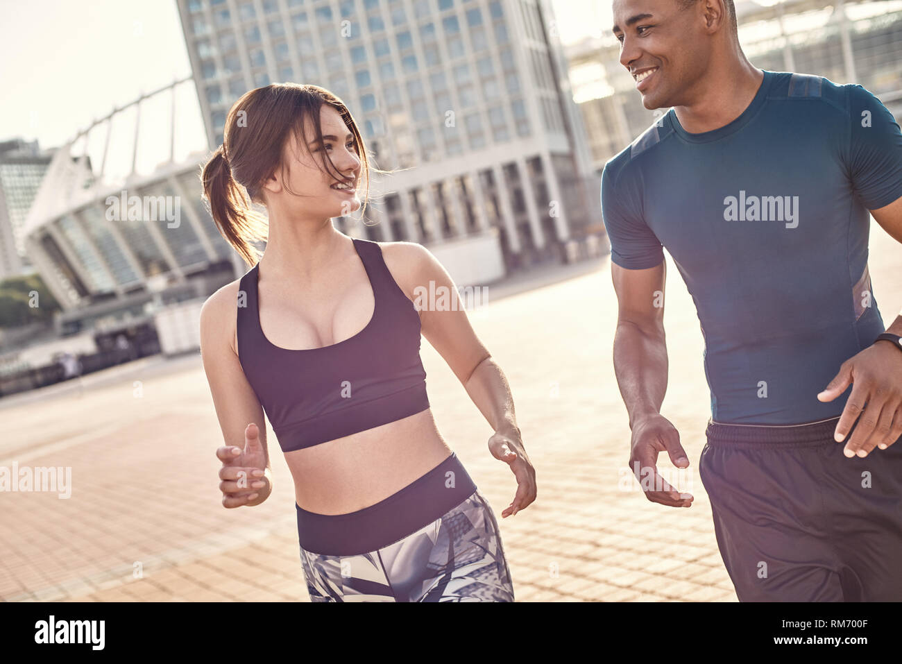 Comune hobby. Giovane e felice coppia multirazziale in esecuzione attraverso strade soleggiato al mattino. Un sano giovane. Sport concetto di motivazione. Concetto di fitness. Donne bellezza. La vita sana. Esercitare insieme Foto Stock