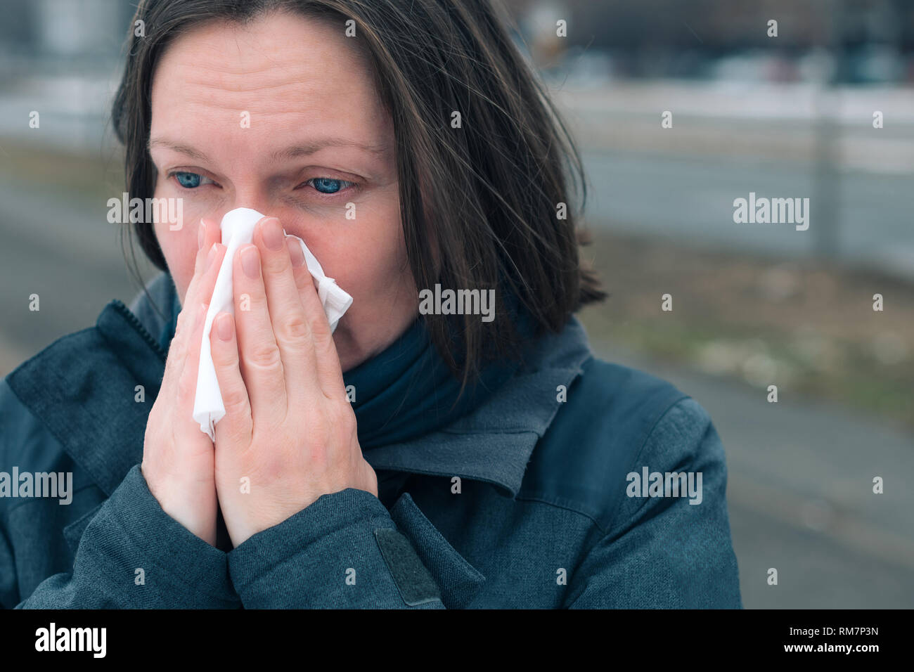 Donna soffia il naso in un fazzoletto di carta per strada in una fredda giornata invernale all'inizio della stagione influenzale Foto Stock