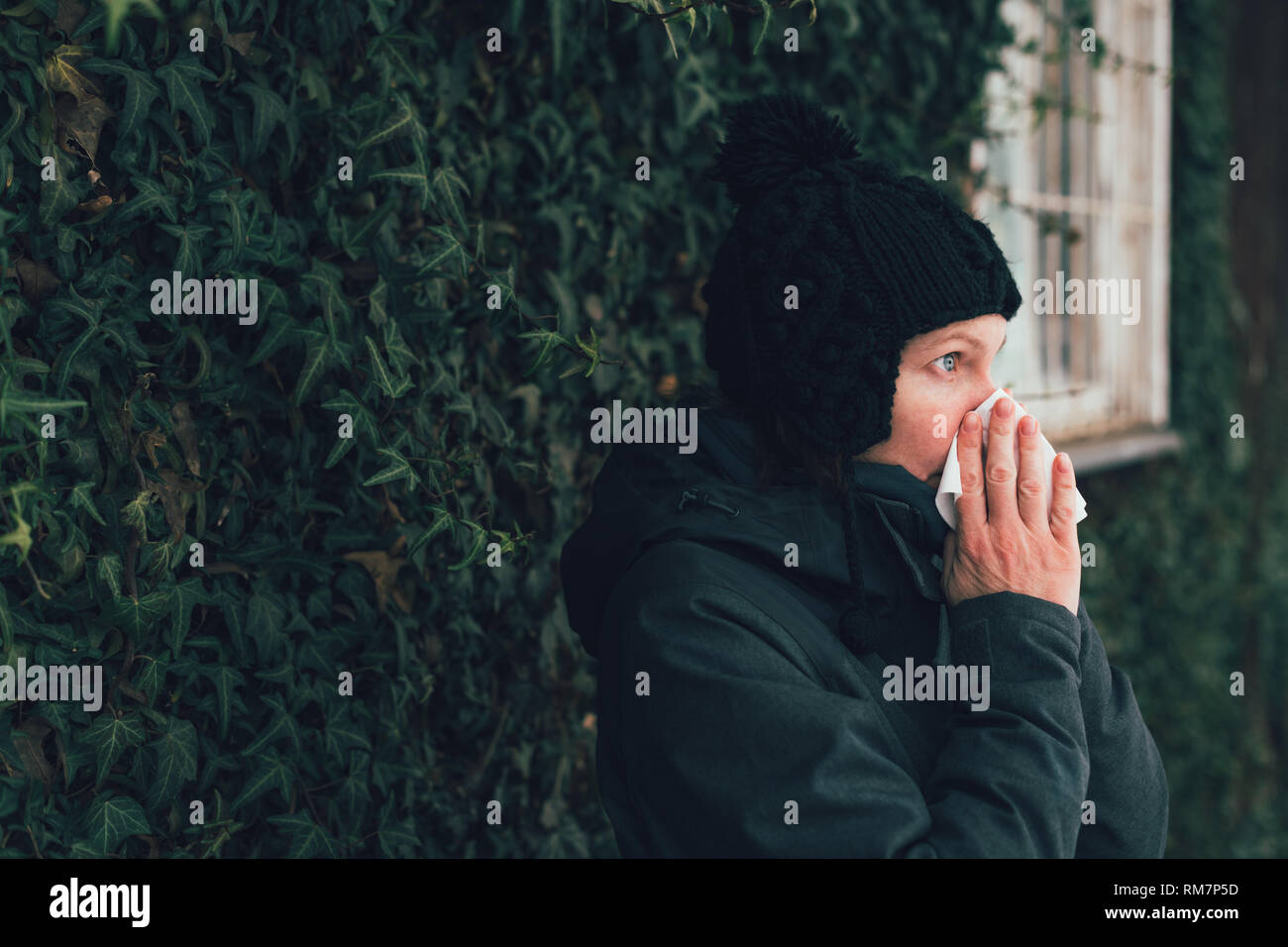Donna soffia il naso in un fazzoletto di carta per strada in una fredda giornata invernale all'inizio della stagione influenzale Foto Stock